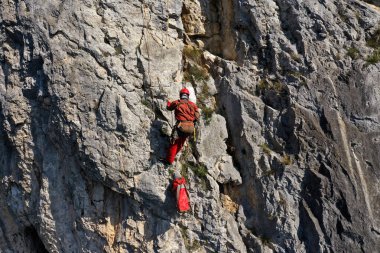 İpe asılı kurtarma operasyonları yapan bir dağcının hava görüntüsü.