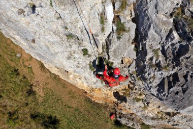 Aerial view of mountain rescue exercise on a rocky wall, rescuer hanging on rope clipart