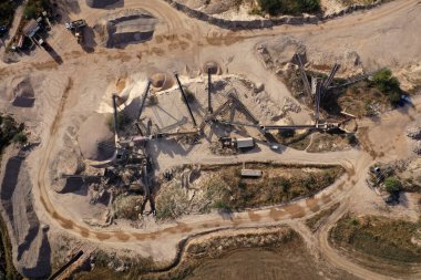 Kazıcının hava görüntüsü ezilmiş taş ocağındaki bir çöp kamyonuna taş yüklüyor.