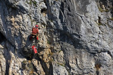 Dağ kurtarıcısının kayalık bir duvarda ipte sallanışını gösteren hava görüntüsü.