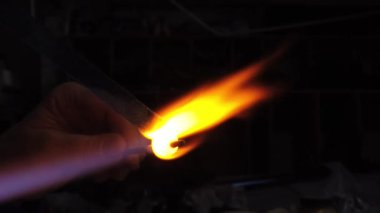 Sanatçı ellerinin yavaş çekim görüntüsü lamba çalışma tekniğiyle cam kolye yaratıyor. Gaz ocağı kullanarak cam ve alevi şekillendirmek.