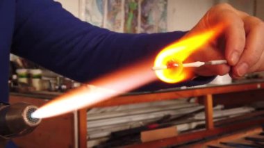 Sanatçı ellerinin yavaş çekim görüntüsü lamba çalışma tekniğiyle cam kolye yaratıyor. Gaz ocağı kullanarak cam ve alevi şekillendirmek.