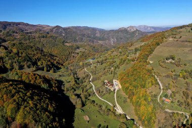 Dağlardaki köy toprak yolunun havadan görünüşü. Sonbahar ormanı ve kırsal çayır insansız hava aracıyla