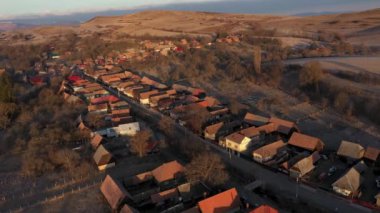 Sabahın erken saatlerinde köy evlerinin üzerinde gün doğumu ışıkları, hava aracı manzarası.