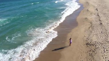  Kumsalda yürüyen muhteşem sarışın bir kadının yavaş çekim görüntüsü. Deniz dalgaları kumlu kıyı şeridini yıkıyor