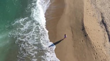  Kumsalda yürüyen muhteşem sarışın bir kadının yavaş çekim görüntüsü. Deniz dalgaları kumlu kıyı şeridini yıkıyor