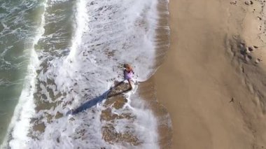  Kumsalda yürüyen muhteşem sarışın bir kadının yavaş çekim görüntüsü. Deniz dalgaları kumlu kıyı şeridini yıkıyor