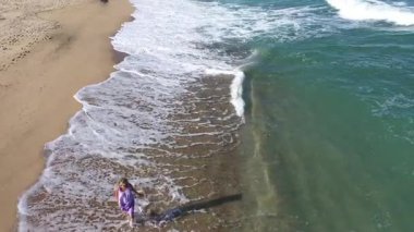 Kumsalda yürüyen muhteşem sarışın bir kadının yavaş çekim görüntüsü. Deniz dalgaları kumlu kıyı şeridini yıkıyor