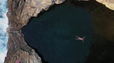  Yunanistan 'ın Thassos adasında, deniz kenarındaki doğal havuz olan Giola gölünde yüzen bir kızın havadan yavaş çekim görüntüsünün üzerinde.