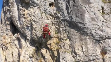 Dağ kurtarıcısının ipte asılı duran kayalık bir duvara tırmanmasını gösteren hava manzarası.