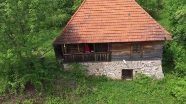 Dağlardaki eski ahşap evin verandasındaki sarışın kadının hava manzarası. 