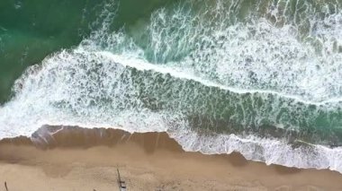 Deniz dalgalarının uzaktan kumlu bir sahile yaklaşan uzaktan görüntüsü.