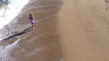   Kumsalda yürüyen muhteşem sarışın bir kadının yavaş çekim görüntüsü. Deniz dalgaları kumlu kıyı şeridini yıkıyor