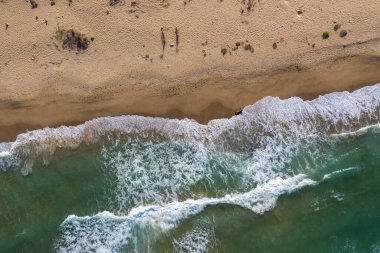 Deniz dalgalarının havadan görünüşü ve uzaktan kumlu bir kumsal.