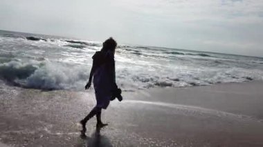 Kumsalda yürüyen sarışın bir manken. Deniz dalgaları kumlu kıyıları yıkıyor