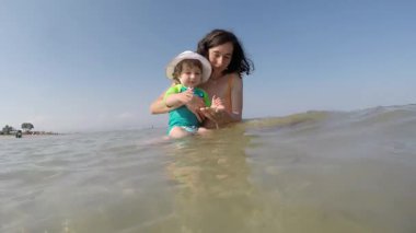 Anne, küçük kızıyla denizde oynuyor.