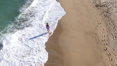  Kumsalda yürüyen muhteşem sarışın bir kadının yavaş çekim görüntüsü. Deniz dalgaları kumlu kıyı şeridini yıkıyor