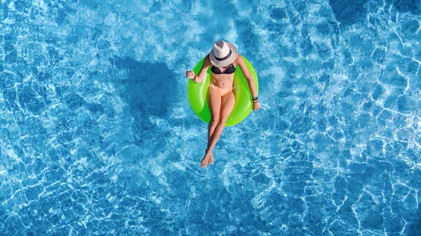 Beautiful woman in hat in swimming pool aerial top view from above, young girl in bikini relaxes and swims on inflatable ring donut and has fun in water on tropical vacation on holiday resort