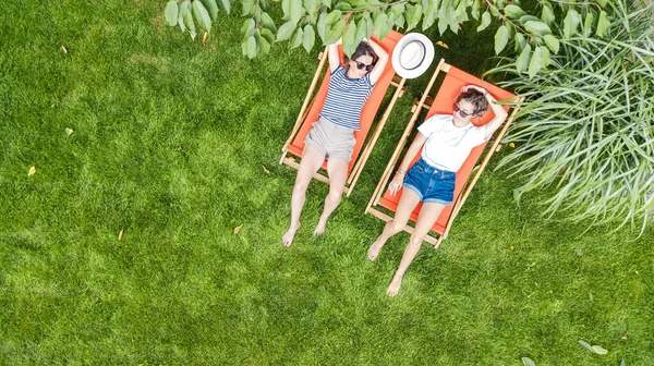 小女孩们在夏日的花园里躺在草地上晒太阳的躺椅里休息 女人们周末在绿地公园里玩得开心 空中俯瞰着天空 免版税图库照片