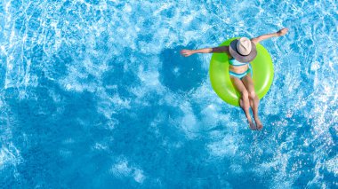 Yüzme havuzundaki aktif genç kız yukarıdan havuz manzaralı, genç kız gevşiyor ve şişme halka donutla yüzüyor ve aile tatilinde suda eğleniyor, tropikal tatil beldesi