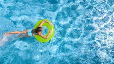 Yüzme havuzundaki aktif genç kız yukarıdan havuz manzaralı, genç kız gevşiyor ve şişme halka donutla yüzüyor ve aile tatilinde suda eğleniyor, tropikal tatil beldesi