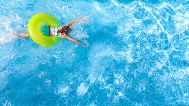 Yüzme havuzundaki aktif genç kız yukarıdan havuz manzaralı, genç kız gevşiyor ve şişme halka donutla yüzüyor ve aile tatilinde suda eğleniyor, tropikal tatil beldesi