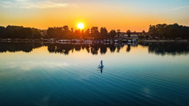 Gün batımında ya da gün doğumunda güzel gölde SUP sörfünde kürek çeken bir kadın Almanya göl bölgesi Mecklenburg 'da sabah macerasında ayakta duruyor.