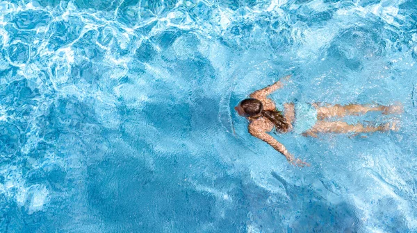 Active girl in swimming pool aerial drone view from above, young woman swims in blue water, tropical vacation, holiday on resort concept