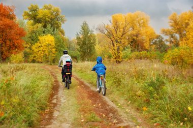 Altın sonbahar parkında aile bisikleti, aktif baba ve çocuklar bisiklet sürüyor, aile sporu ve çocuklarla açık havada spor yapıyor.