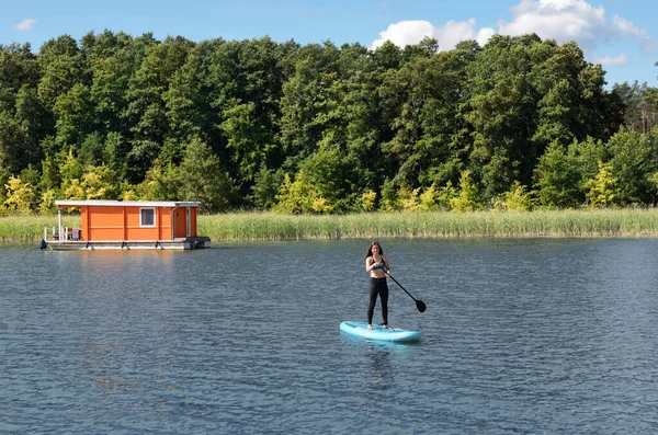 Girl paddling on SUP board on beautiful lake, standing up paddle boarding adventure in Germany lake district Mecklenburg