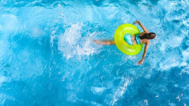 Yüzme havuzundaki aktif genç kız yukarıdan havuz manzaralı, genç kız gevşiyor ve şişme halka donutla yüzüyor ve aile tatilinde suda eğleniyor, tropikal tatil beldesi