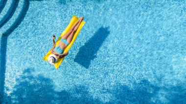 Beautiful woman in hat in swimming pool aerial drone view from above, young girl in bikini relaxes and swims on inflatable mattress and has fun in water on vacation, tropical holiday resort