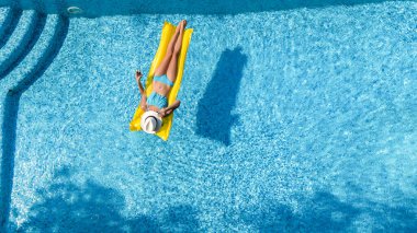 Beautiful woman in hat in swimming pool aerial drone view from above, young girl in bikini relaxes and swims on inflatable mattress and has fun in water on vacation, tropical holiday resort