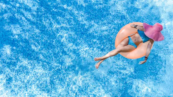 Beautiful woman in hat in swimming pool aerial drone view from above, young girl in bikini relaxes and swims on inflatable ring donut and has fun in water on tropical vacation on holiday resort