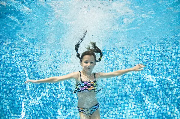 Child swims underwater in swimming pool, active little girl jumps, dives and has fun under water, kid fitness and sport on family vacation