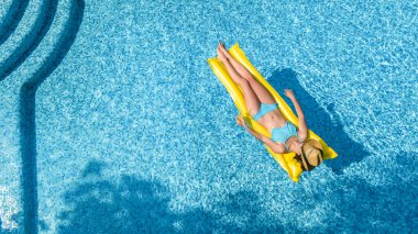 Yüzme havuzunda şapkalı güzel bir kadın yukarıdan drone manzaralı, bikinili genç bir kız şişme yatakta dinleniyor ve yüzüyor, genç kız tatilde suda eğleniyor, tropikal tatil beldesi.