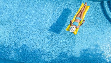 Yüzme havuzunda şapkalı güzel bir kadın yukarıdan drone manzaralı, bikinili genç bir kız şişme yatakta dinleniyor ve yüzüyor, genç kız tatilde suda eğleniyor, tropikal tatil beldesi.