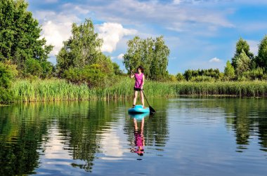 Aktif bir kadın güzel göl üzerinde kürek çekiyor, yaz ormanı manzarası ve arka planda doğa, açık havada kürek çeken su macerası, spor ve sağlıklı yaşam tarzı kavramı