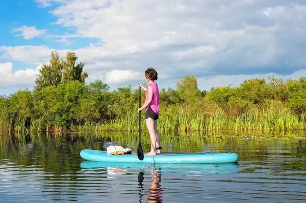 Aktif bir kadın güzel göl üzerinde kürek çekiyor, yaz ormanı manzarası ve arka planda doğa, açık havada kürek çeken su macerası, spor ve sağlıklı yaşam tarzı kavramı