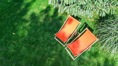 Güneş yatağı sandalyeli yaz bahçesi çimenlerin üstünde gökyüzü manzaralı, yeşil park ağaçları ve yukarıdan rahatlamak için bir yer.