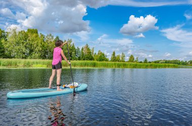 Aktif kadın güzel göl ya da nehir üzerinde SUP sörfü yapıyor, yaz ormanı manzarası ve arka planda doğa, açık havada kürek çeken su macerası, spor ve sağlıklı yaşam tarzı kavramı