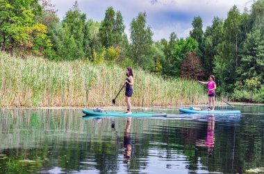 SUP 'de aktif bir aile, anne ve kız nehir suyunda kürek çekiyor, yaz aile sporu yatak tahtalarında
