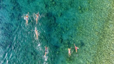 Turkuaz denizde yüzen insanların hava aracı görüntüsü, temiz suda eğitim gören bir grup yüzücü, açık denizde yüzme ve triatlon sporu.