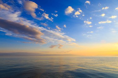 Deniz ve dağların üzerinde güzel bulutlu gün batımı. Turuncu güneşin ışınlarında parlak bir gökyüzü. Doğal