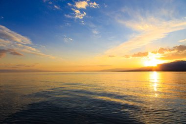 Denizde renkli bir gün batımı. Turuncu güneş ışınlarında dağ gölü. Kırgızistan, Issyk-Kul Gölü. doğal arkaplan