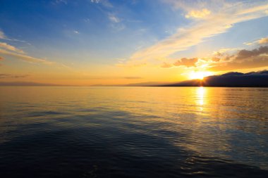 Denizde renkli bir gün batımı. Turuncu güneş ışınlarında dağ gölü. Kırgızistan, Issyk-Kul Gölü. doğal arkaplan