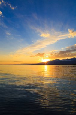 Denizde renkli bir gün batımı. Turuncu güneş ışınlarında dağ gölü. Kırgızistan, Issyk-Kul Gölü. doğal arkaplan