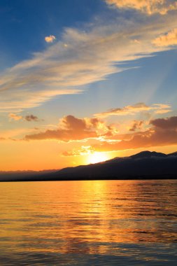 Denizde renkli bir gün batımı. Turuncu güneş ışınlarında dağ gölü. Kırgızistan, Issyk-Kul Gölü. doğal arkaplan