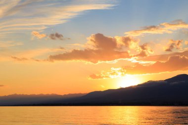 Denizde renkli bir gün batımı. Turuncu güneş ışınlarında dağ gölü. Kırgızistan, Issyk-Kul Gölü. doğal arkaplan