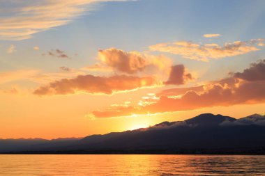 Dağların üzerinde renkli deniz plajı. Gün doğumu. Derin mavi gökyüzü ve güneş ışınları. Doğal arka plan. Turuncu güneşin ışınlarında parlak gökyüzü.